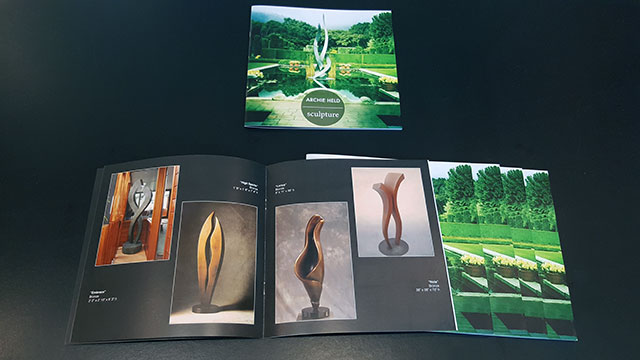 An image of Archie Held's catalog. Titled Sculpture with an image of Entice on the front. Multiple copies shown below. One opened to the middle page showing Embrace, High Spirits, Lorica and Nola